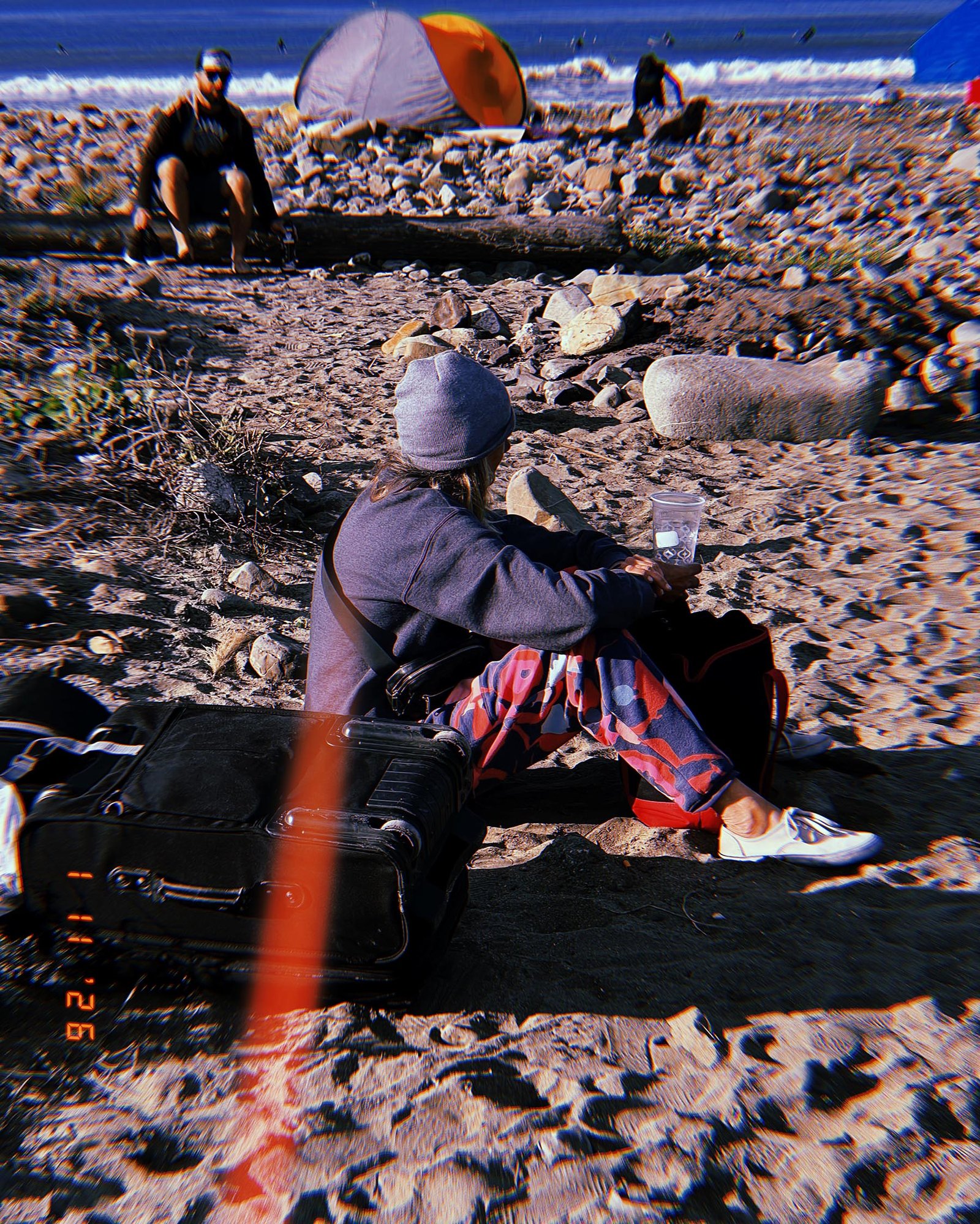 person sitting on rocky beach with suitcase and tent near ocean in San Francisco