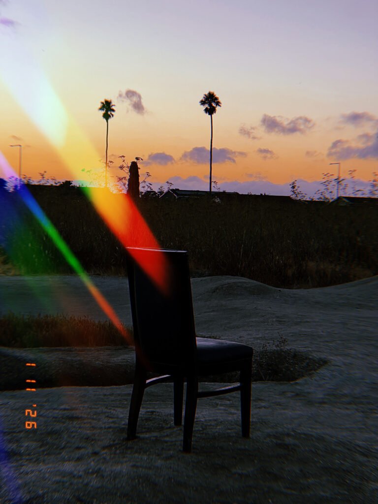 empty chair in open landscape at sunset with palm trees and rainbow light leak
