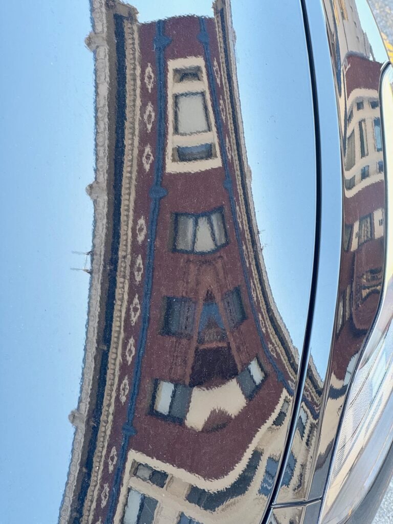 distorted reflection of a historic building facade in curved car surface