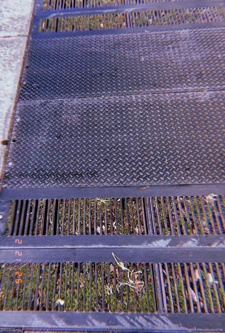 large metal sidewalk access hatch surrounded by drainage grates
