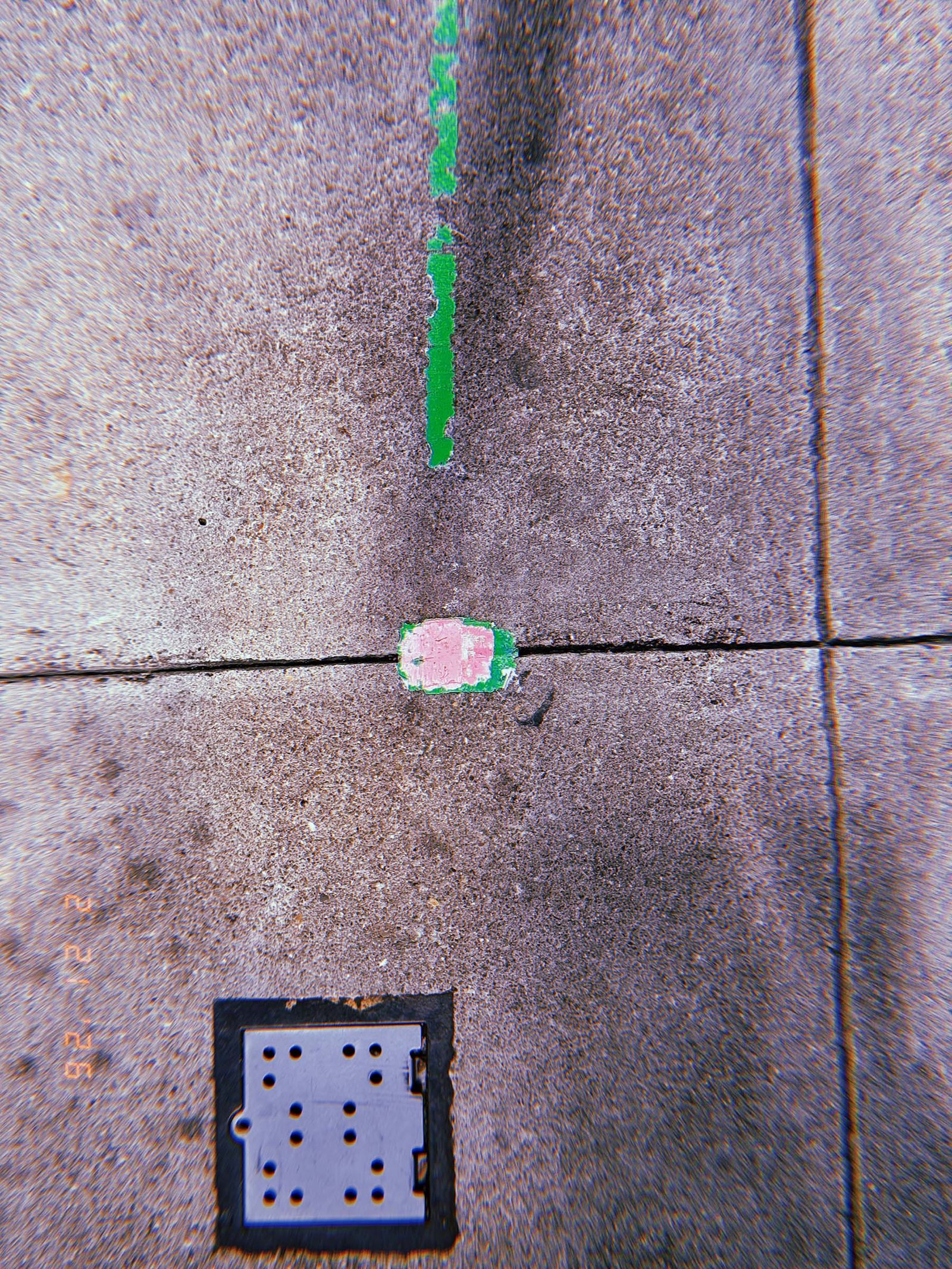 green survey marking line leading to a small painted utility marker on sidewalk