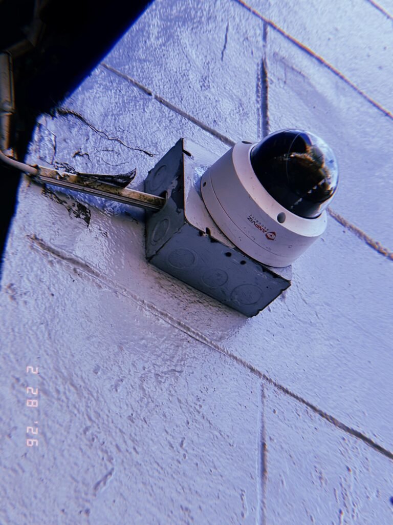 dome surveillance camera mounted on metal junction box with exposed conduit on painted wall