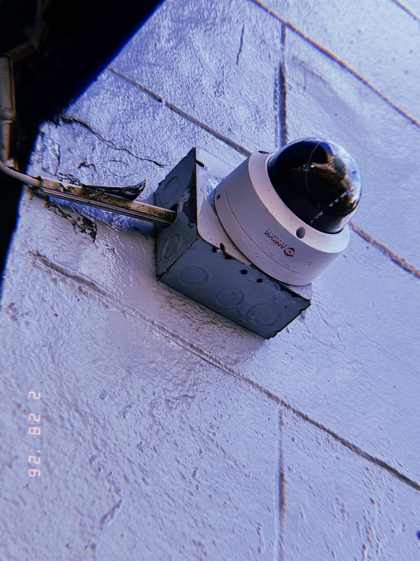 dome surveillance camera mounted on metal junction box with exposed conduit on painted wall