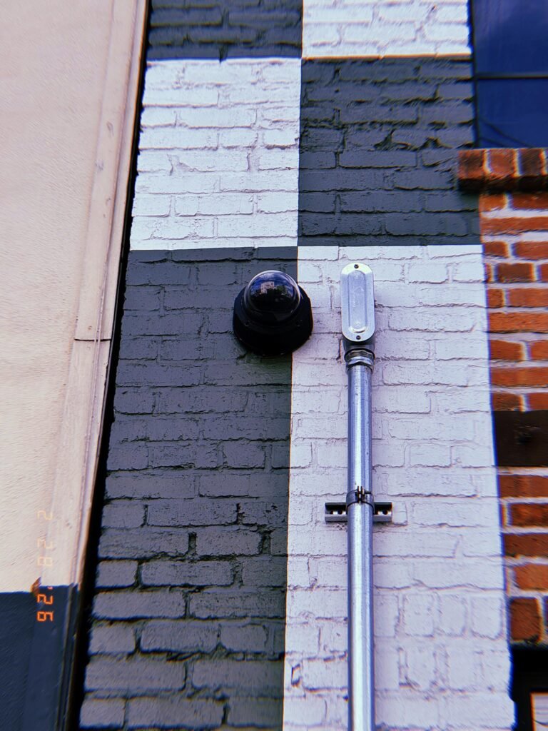 dome surveillance camera mounted on painted brick wall beside vertical conduit pipe