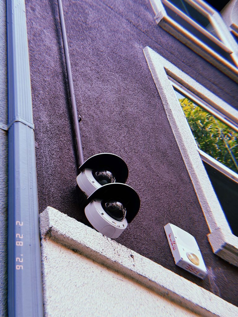 two wall-mounted dome surveillance cameras with protective hoods installed near window and fire alarm unit