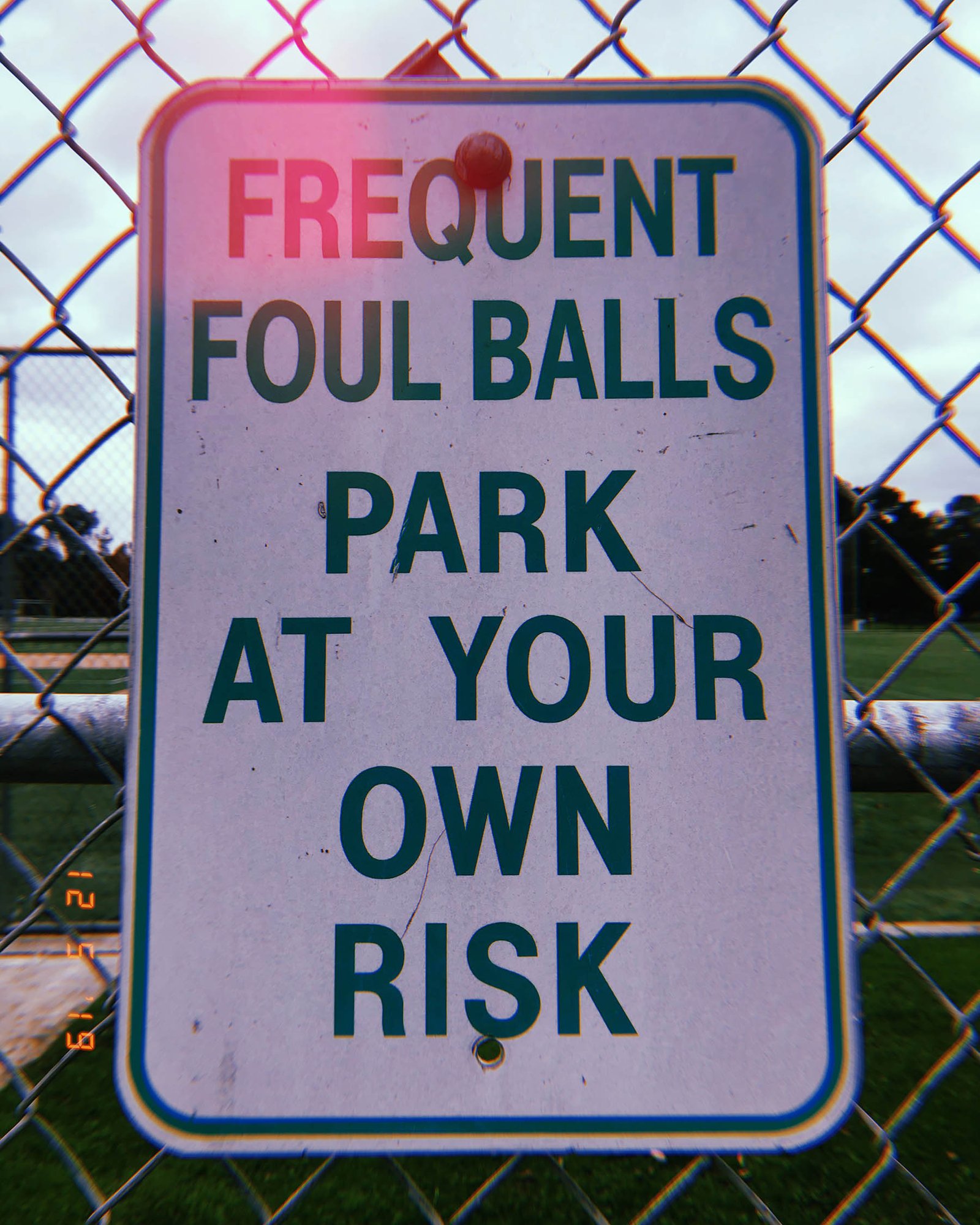 warning sign on chain link fence reading frequent foul balls park at your own risk