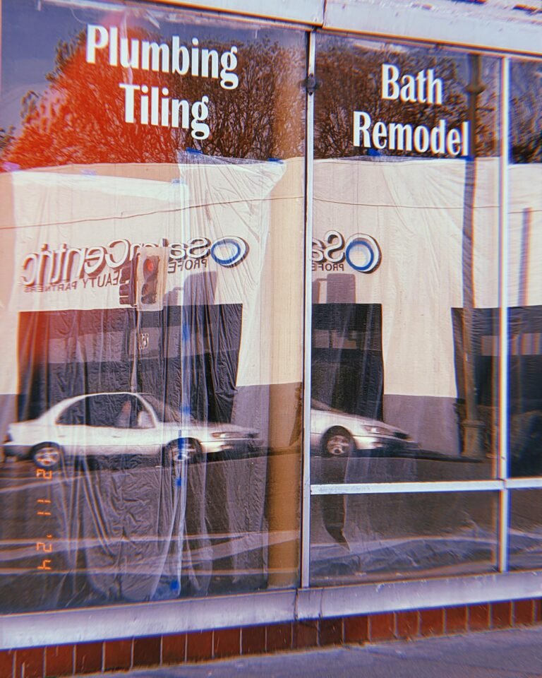 storefront window reflecting street traffic with signs reading plumbing tiling and bath remodel