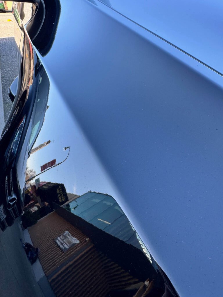 buildings and street sign reflected in dark blue car body