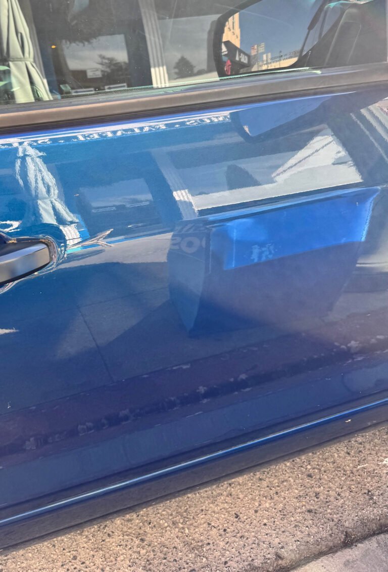 reflection of building facade and sidewalk in blue car door surface