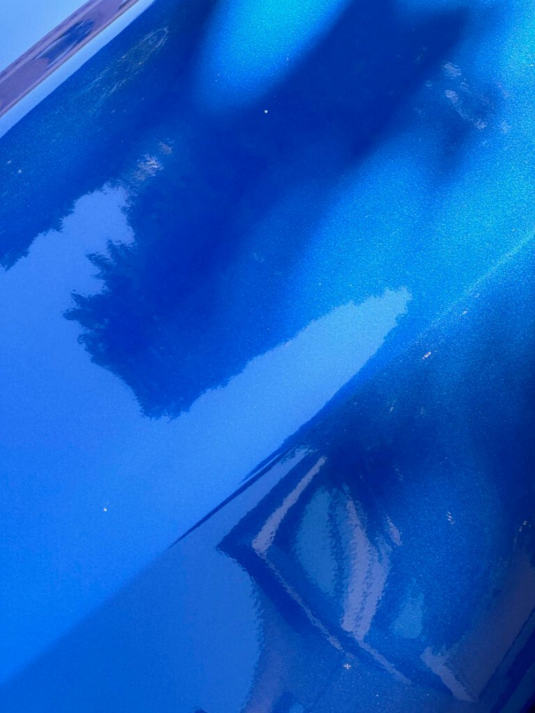 reflection of tree canopy and sky in metallic blue car surface
