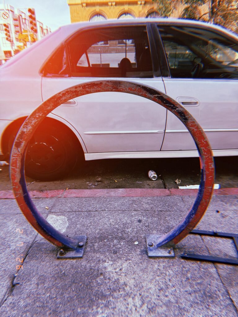 parked car framed through a circular bicycle rack on the sidewalk