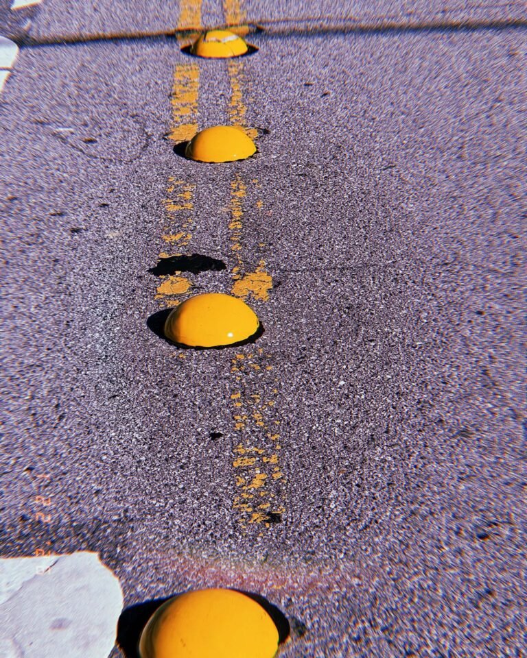row of yellow reflective road studs aligned along a worn center line