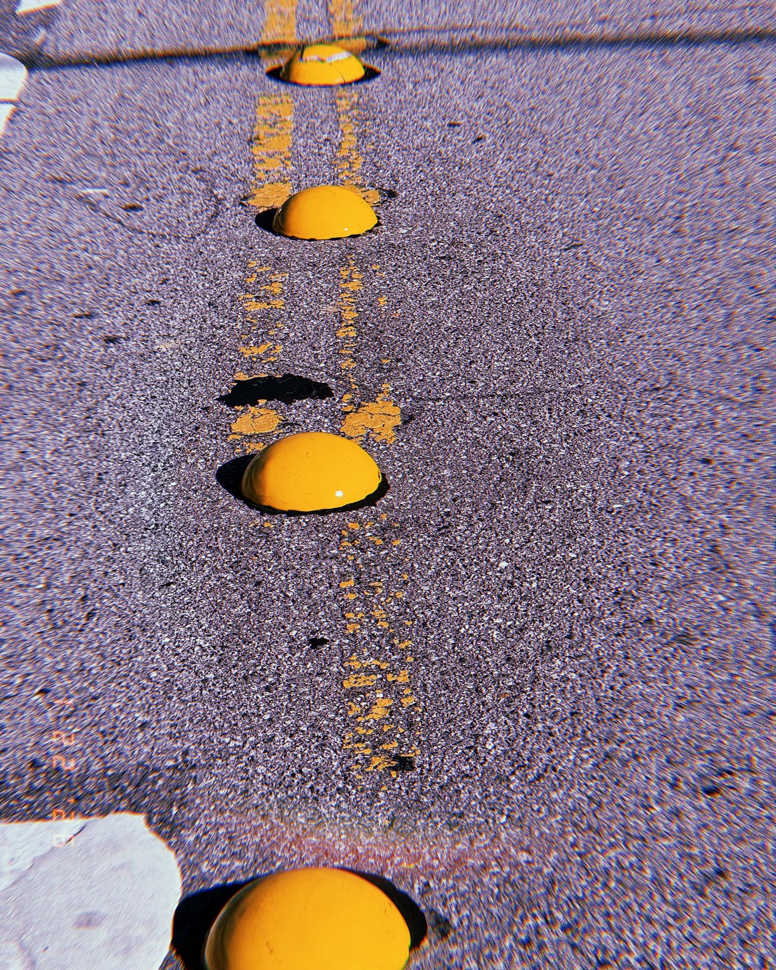 row of yellow reflective road studs aligned along a worn center line
