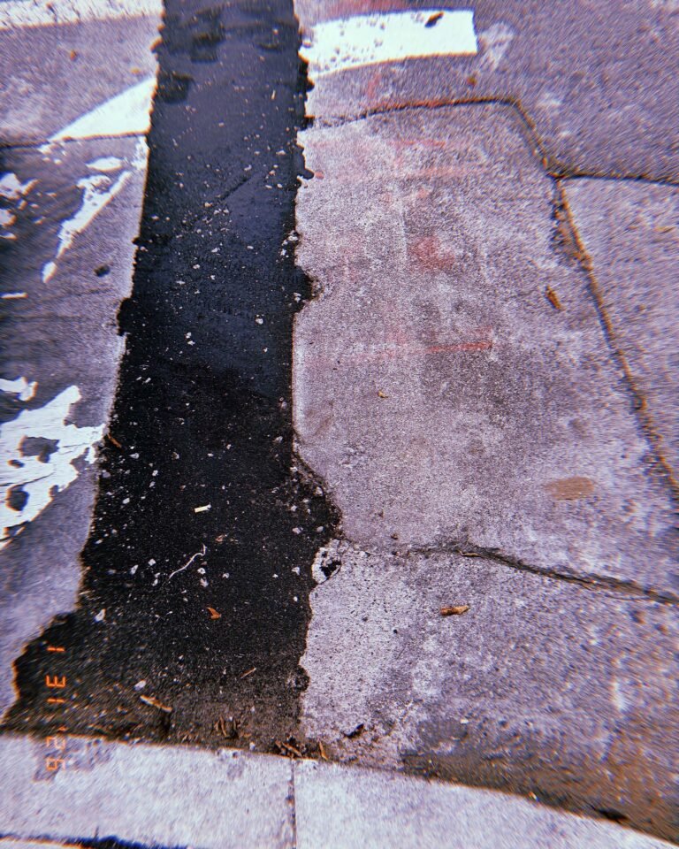 strip of dark asphalt repair cutting through older concrete sidewalk slabs