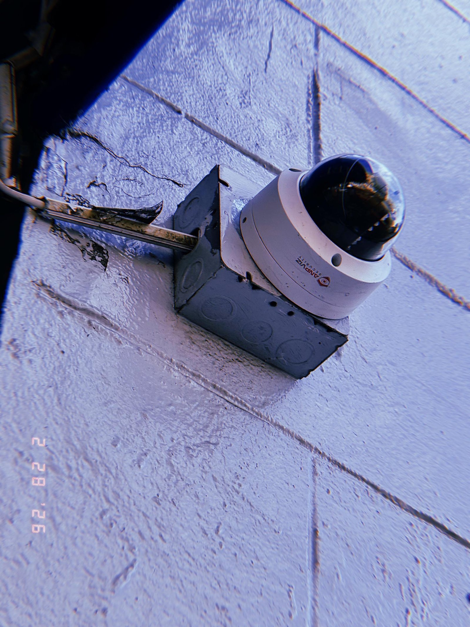 dome surveillance camera mounted on metal junction box with exposed conduit on painted wall