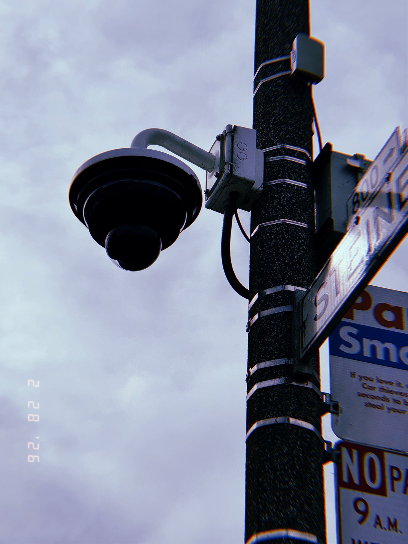 pole-mounted dome surveillance camera with conduit wiring and junction box attached to street sign post