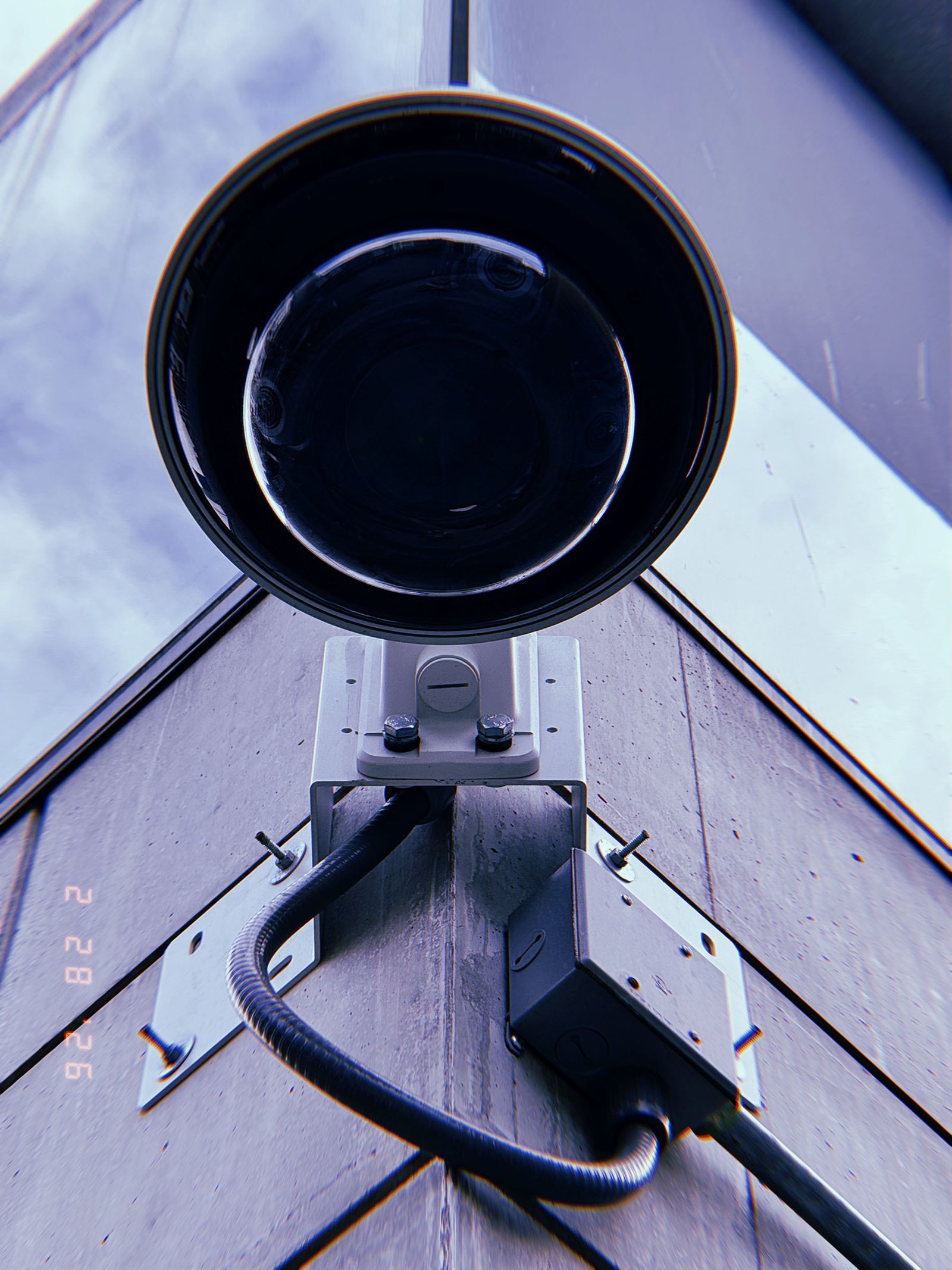 wall-mounted surveillance camera dome with exposed wiring and junction box on building facade