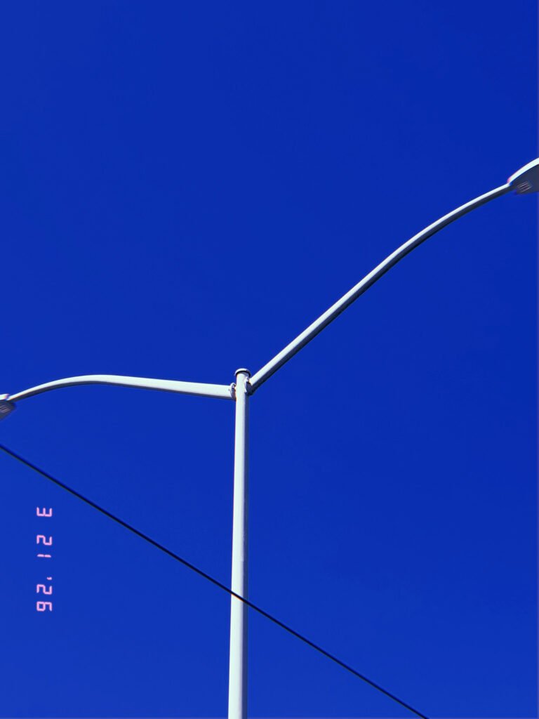 twin street light arms extending from central pole with overhead utility wire against clear sky