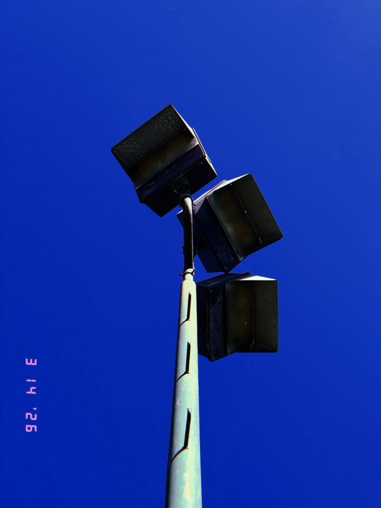 three rectangular floodlight units mounted on angled arm at top of tall pole against clear sky