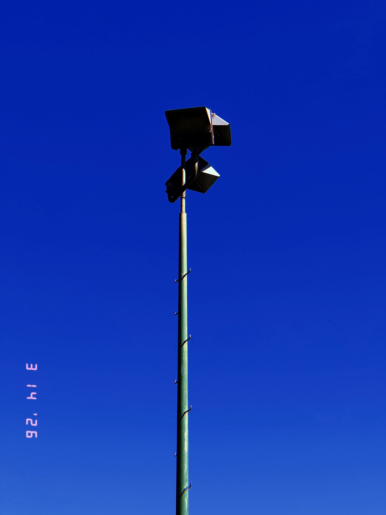 dual floodlight units mounted on tall pole with vertical access pegs against clear sky