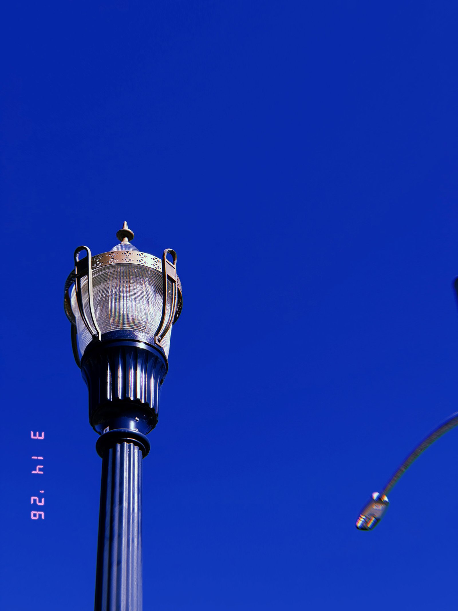 ornamental street lamp with decorative metal housing mounted on vertical pole against clear sky