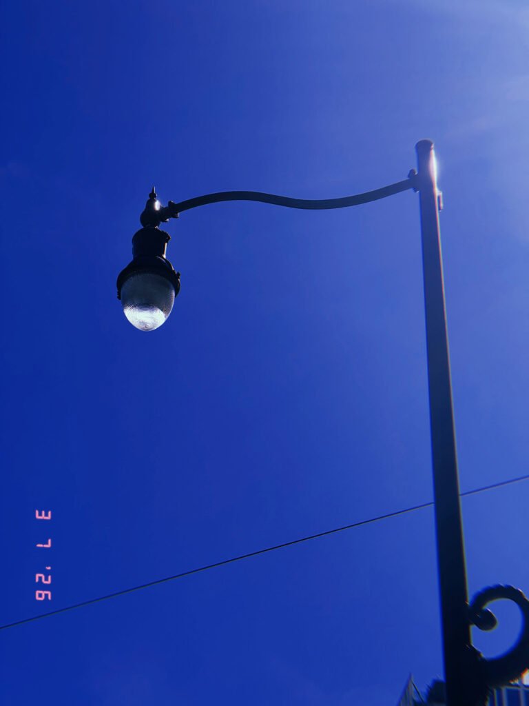 ornamental street lamp with glass enclosure mounted on curved metal arm against clear sky