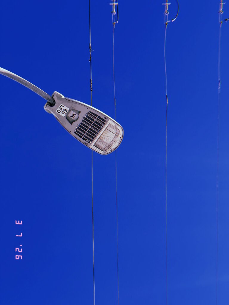 LED street light fixture mounted on curved pole with overhead utility wires against clear sky