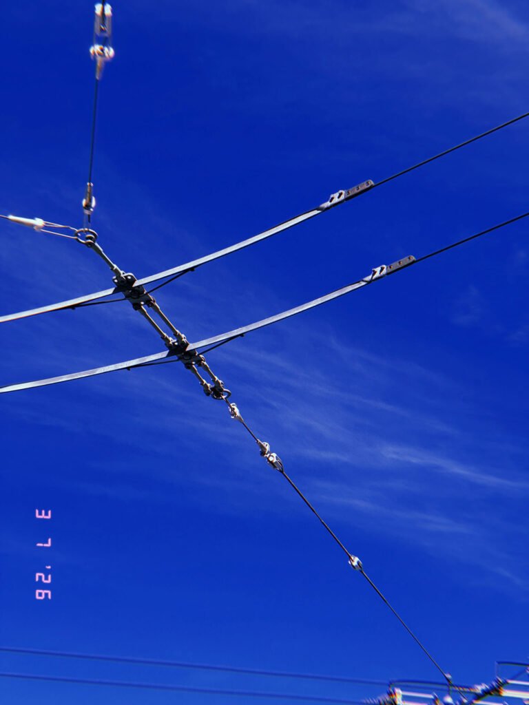 overhead transmission arms and tension cables forming angular connection against blue sky