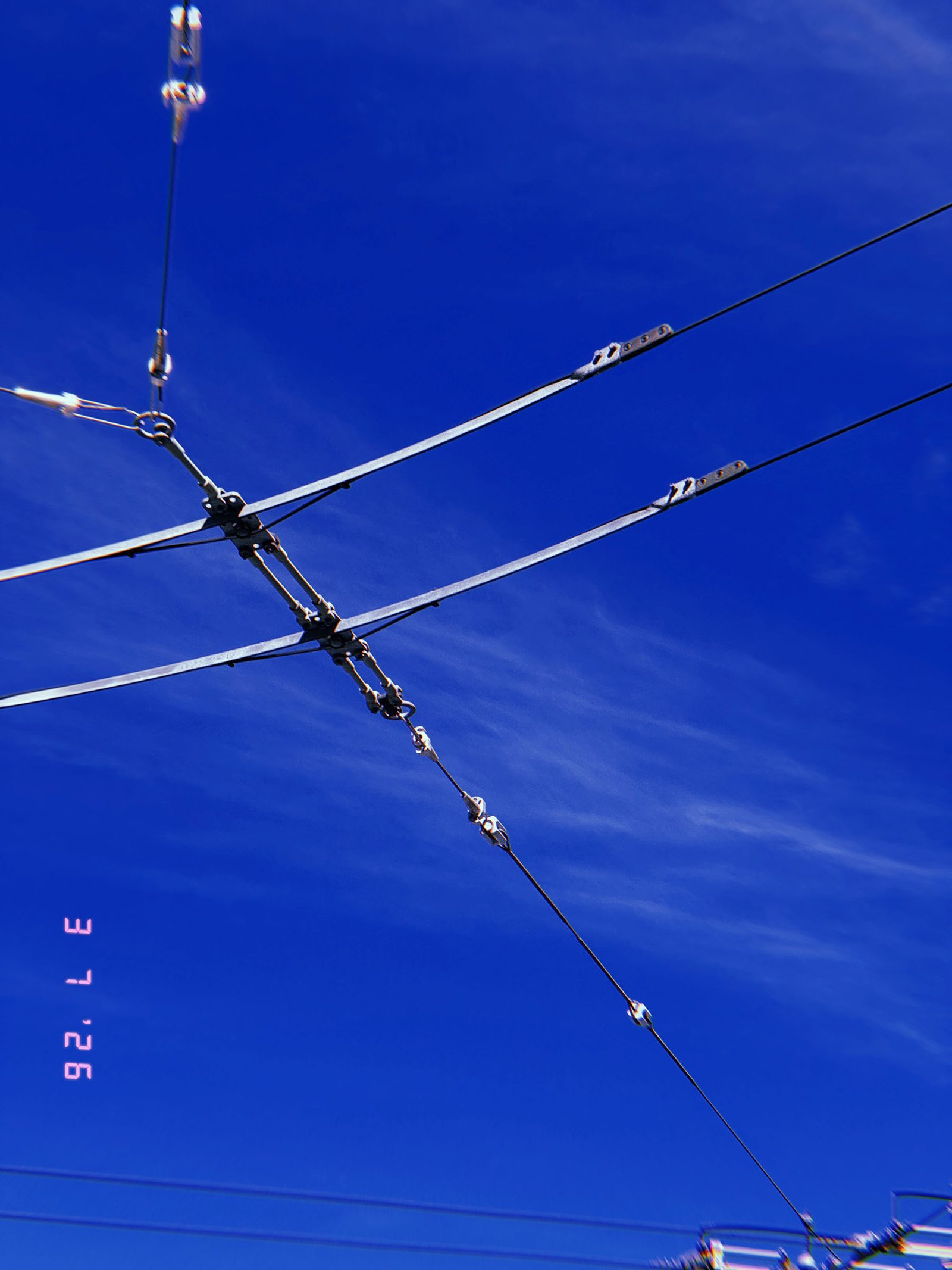 overhead transmission arms and tension cables forming angular connection against blue sky