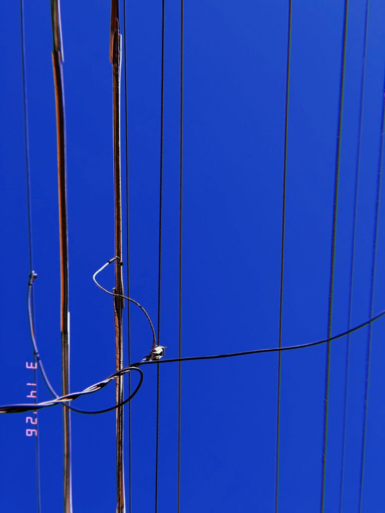 overhead utility wires intersecting with vertical cables against clear blue sky