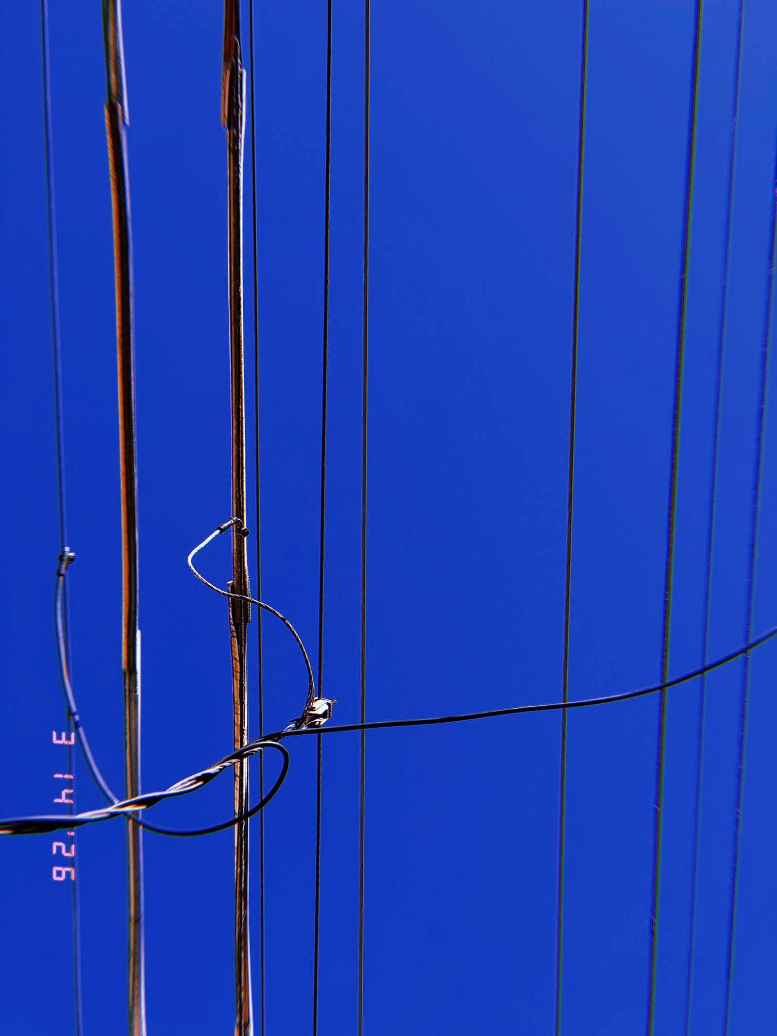 overhead utility wires intersecting with vertical cables against clear blue sky