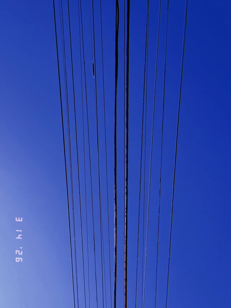 parallel overhead utility wires forming linear transmission pattern against blue sky