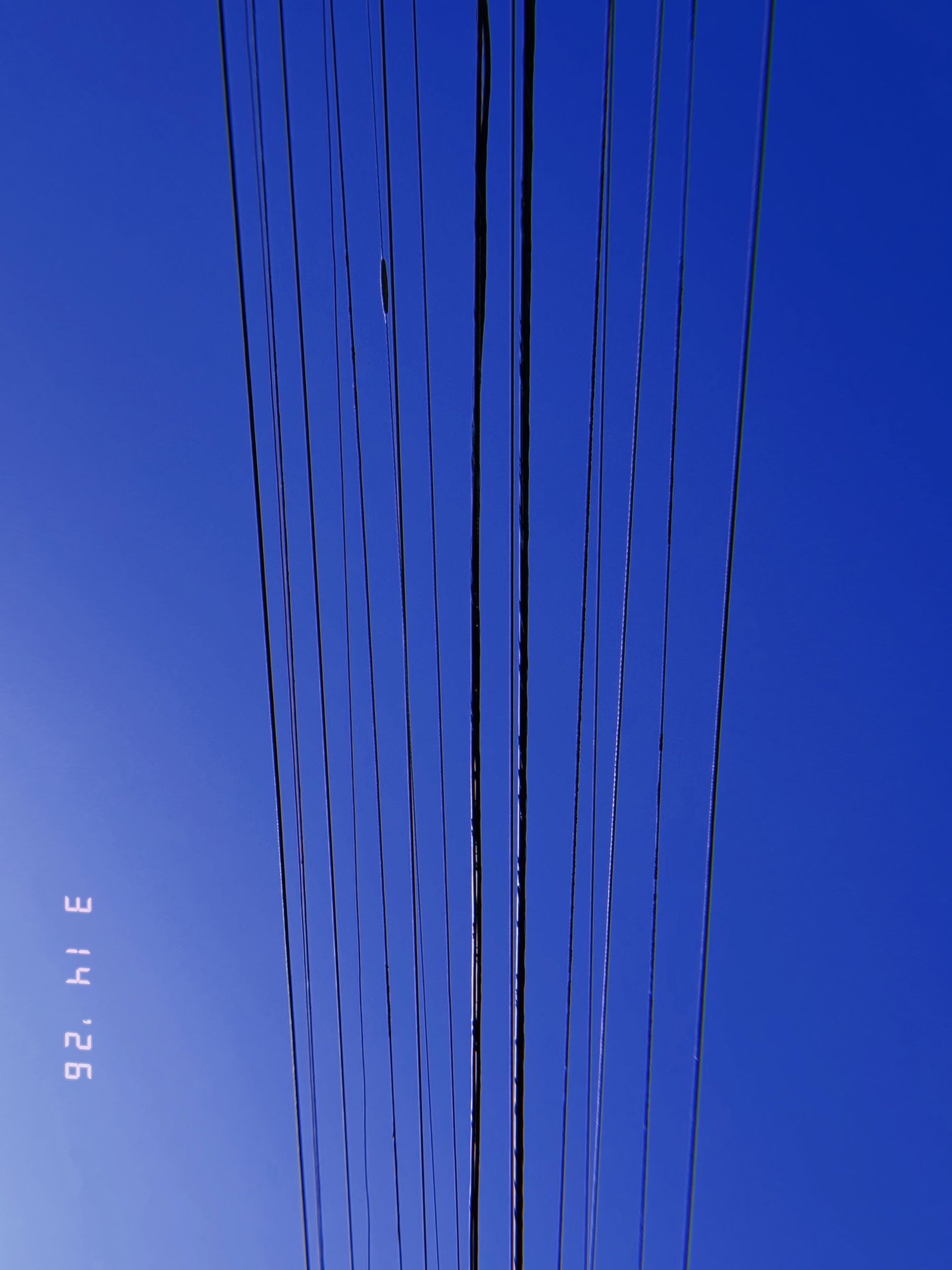 parallel overhead utility wires forming linear transmission pattern against blue sky