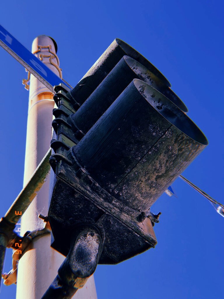 weathered traffic signal with hooded visors mounted on pole against blue sky