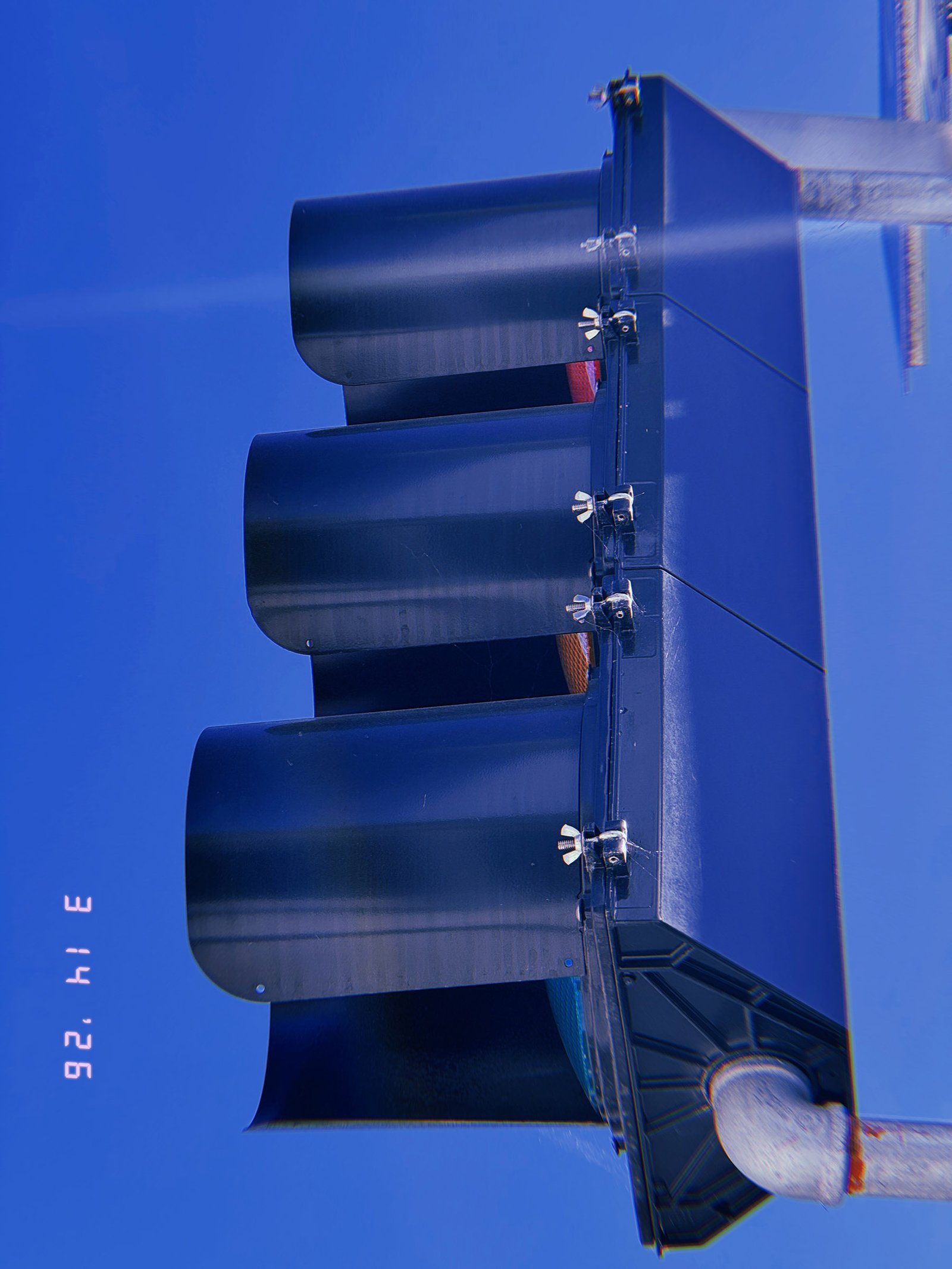 side view of traffic signal lights with hooded visors against blue sky