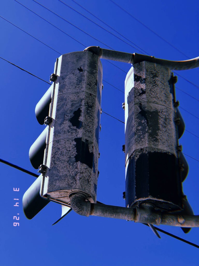 weathered traffic signal housings mounted on pole with visible wiring against blue sky