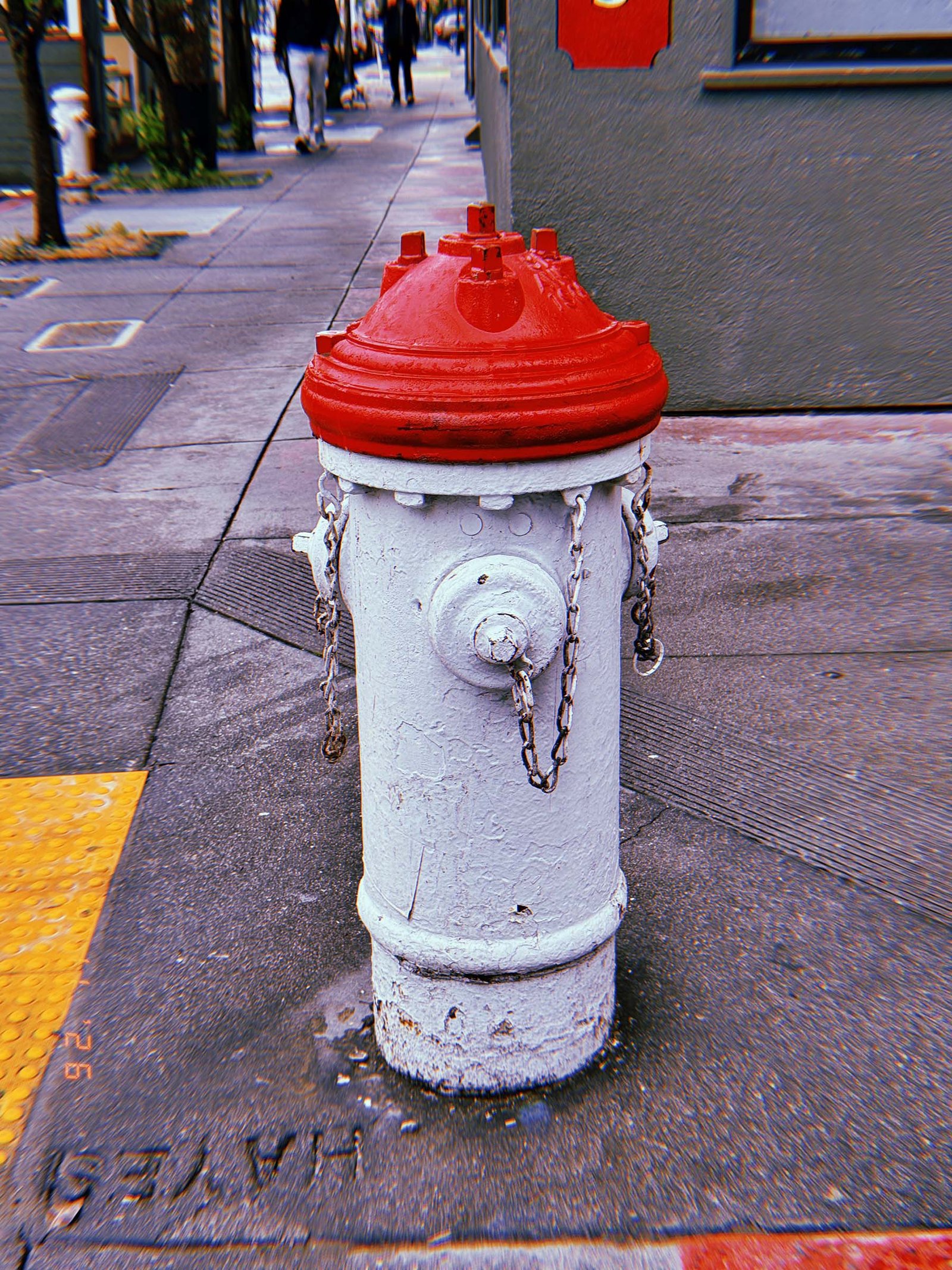 White fire hydrant with red cap standing on a sidewalk corner, with chains hanging from the side outlets and a textured pavement surface around it.