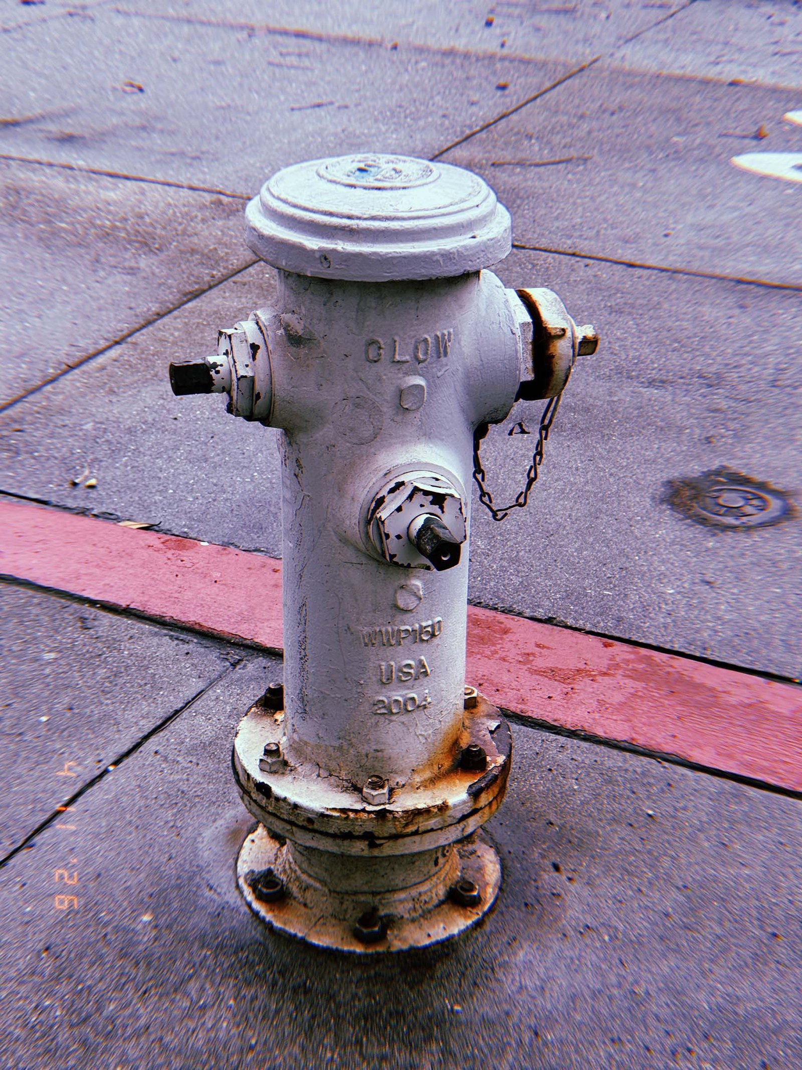 White fire hydrant labeled “LOW” standing on a sidewalk near a red-painted curb, with asphalt road and concrete pavement surrounding it.