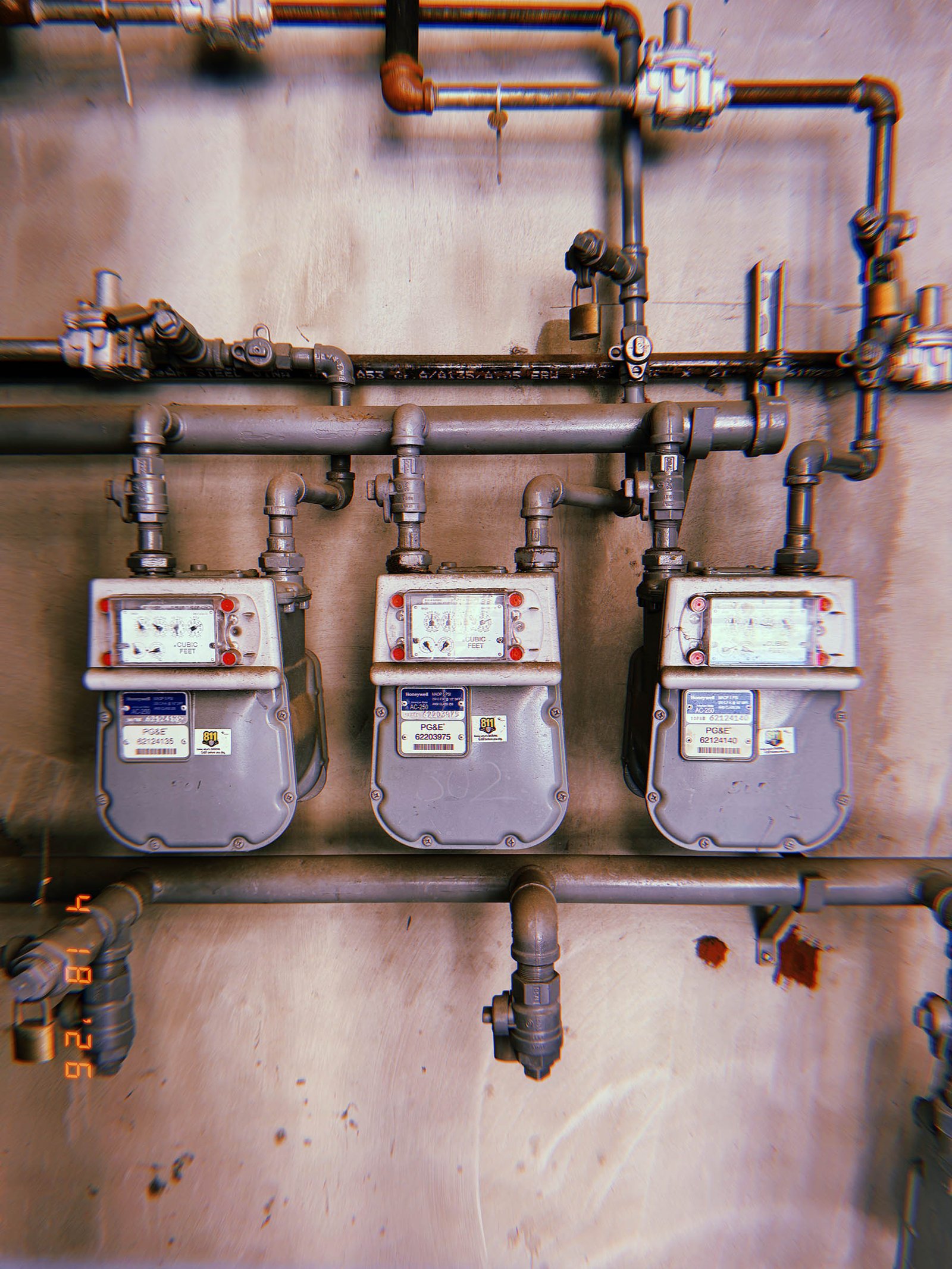 Three residential gas meters mounted in a horizontal row within an exposed pipe distribution system attached to an interior utility wall.