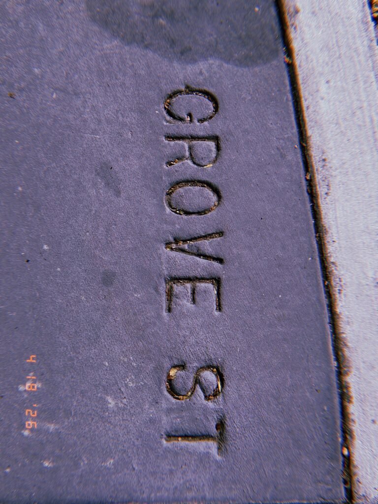 The words "GROVE ST" embedded in a dark concrete sidewalk section as a permanent street identification marker.