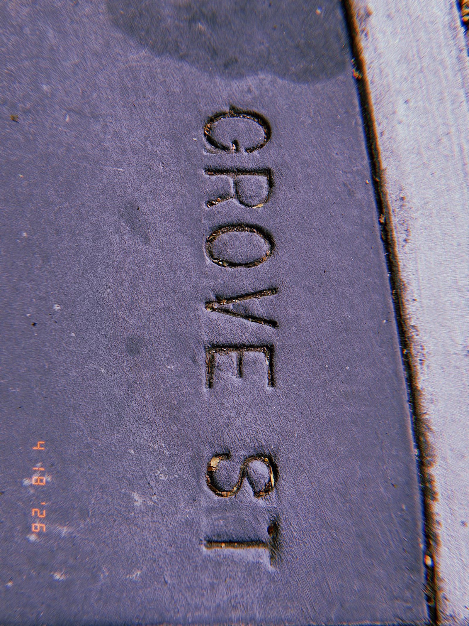 The words "GROVE ST" embedded in a dark concrete sidewalk section as a permanent street identification marker.