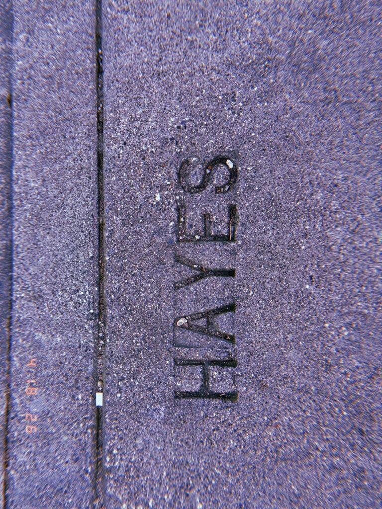 The word "HAYES" embedded in a concrete sidewalk surface as a permanent street identification marker.