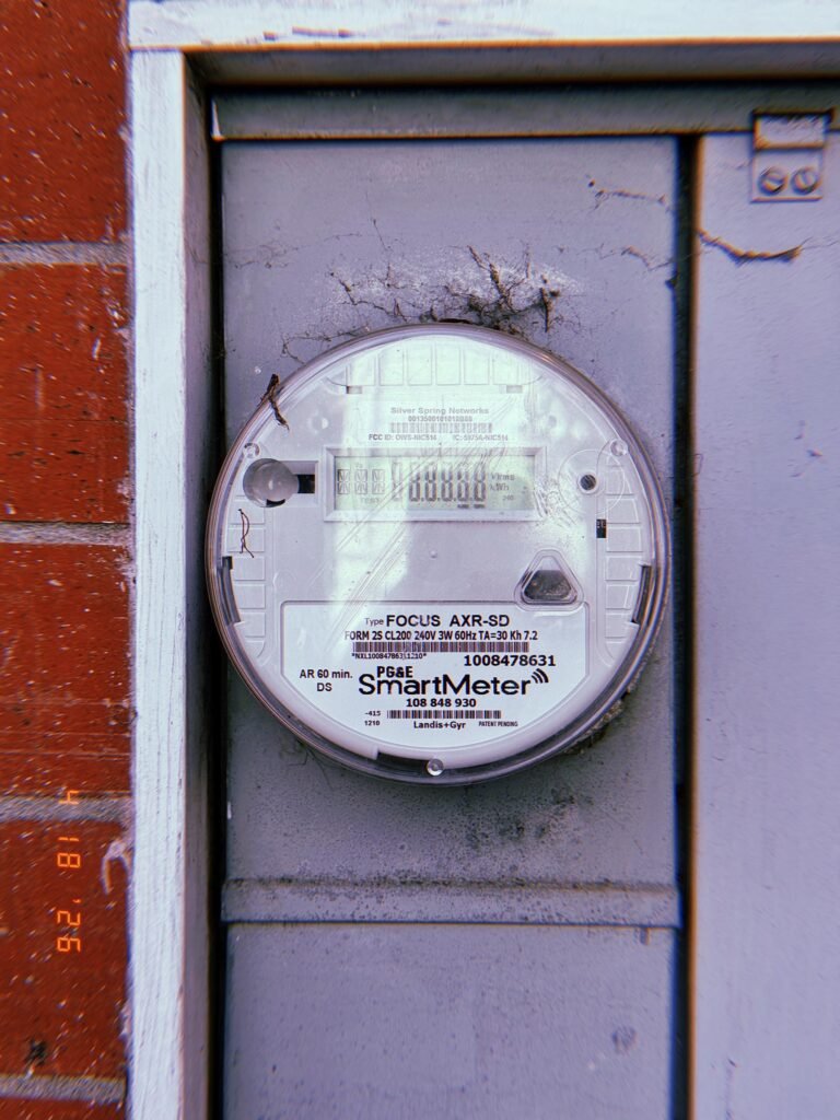 A digital electrical smart meter mounted within a recessed metal utility enclosure, with a display screen and monitoring components integrated into a building electrical service system.