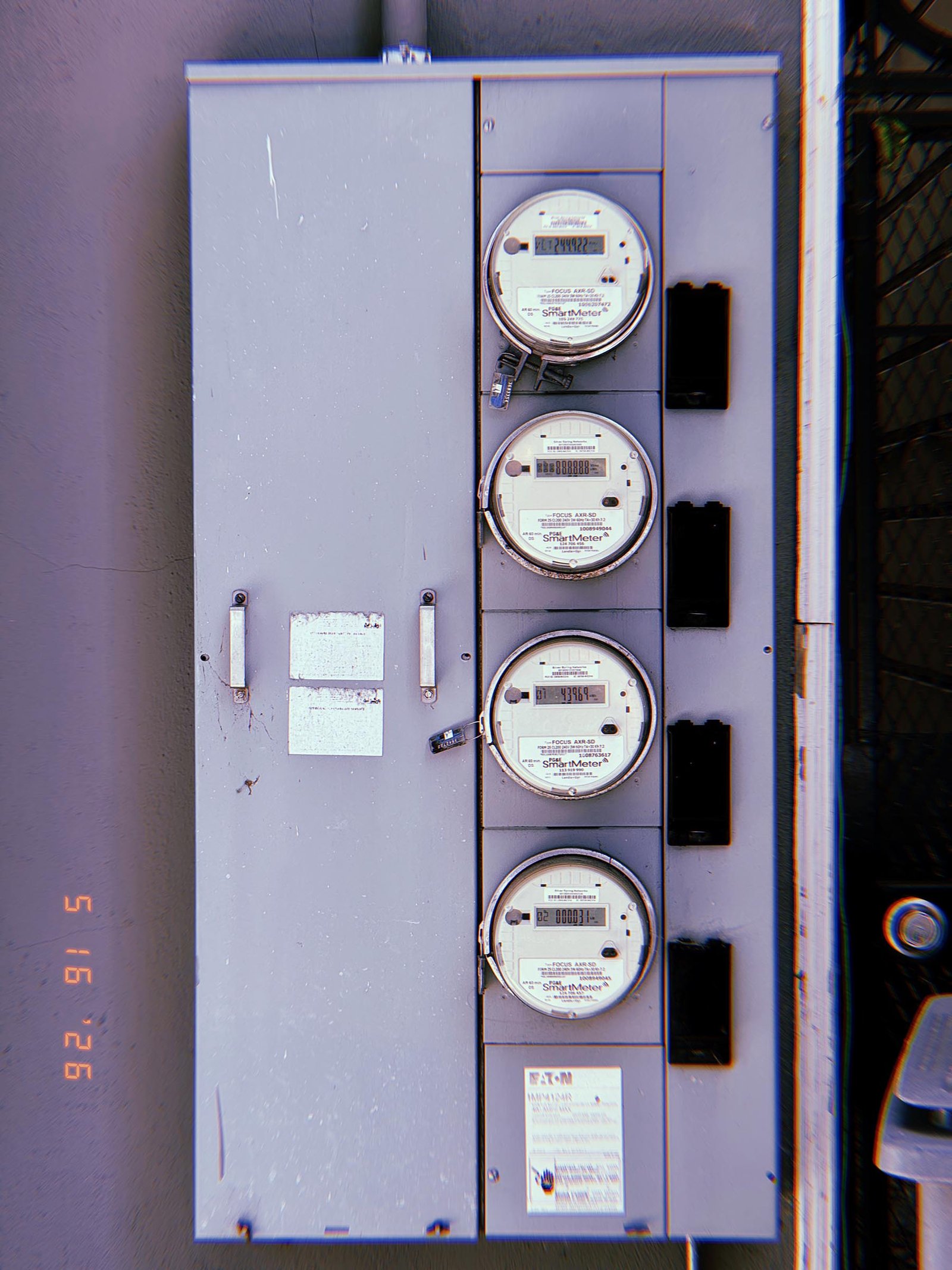 Four digital electrical smart meters mounted vertically within a large utility distribution cabinet, with individual meter displays integrated into a centralized electrical service system.