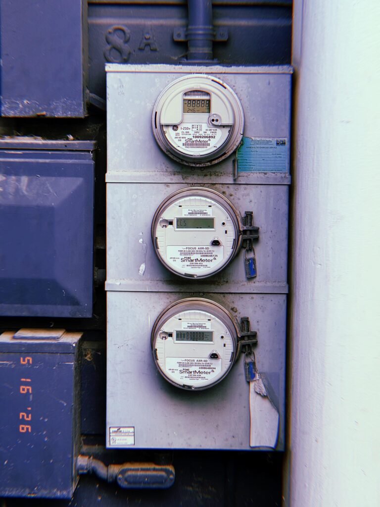 Three digital electrical smart meters mounted vertically inside a metal utility cabinet, with display screens, locking mechanisms, and service enclosures arranged as part of a building electrical distribution system.