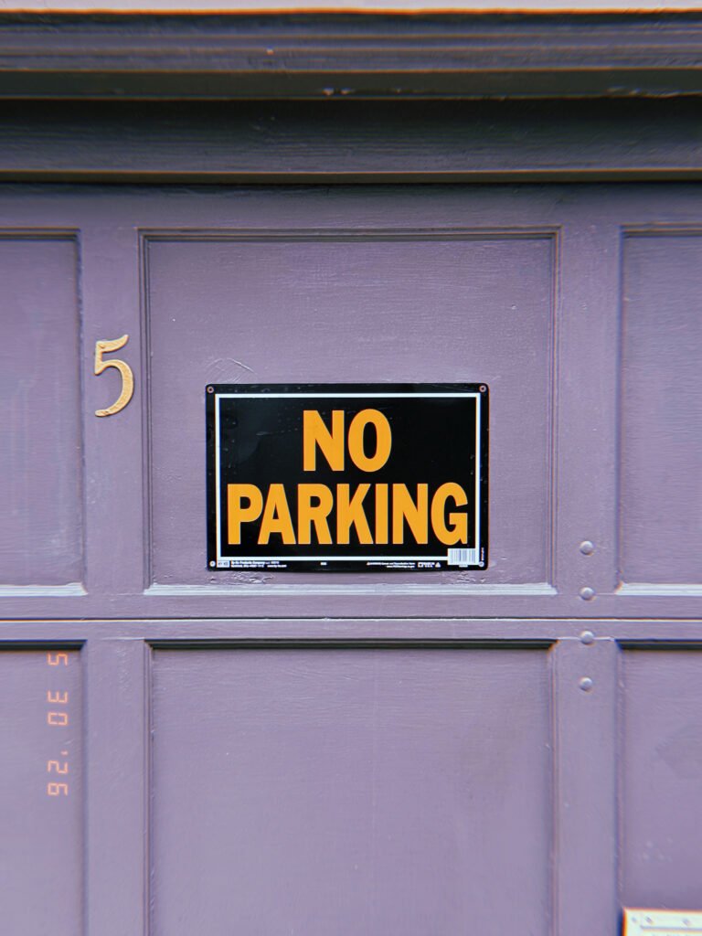 A black and gold “NO PARKING” sign mounted within the recessed center panel of a residential garage door. The sign is positioned beneath a house number and integrated into the door’s geometric structure, marking the driveway as a controlled private access point.
