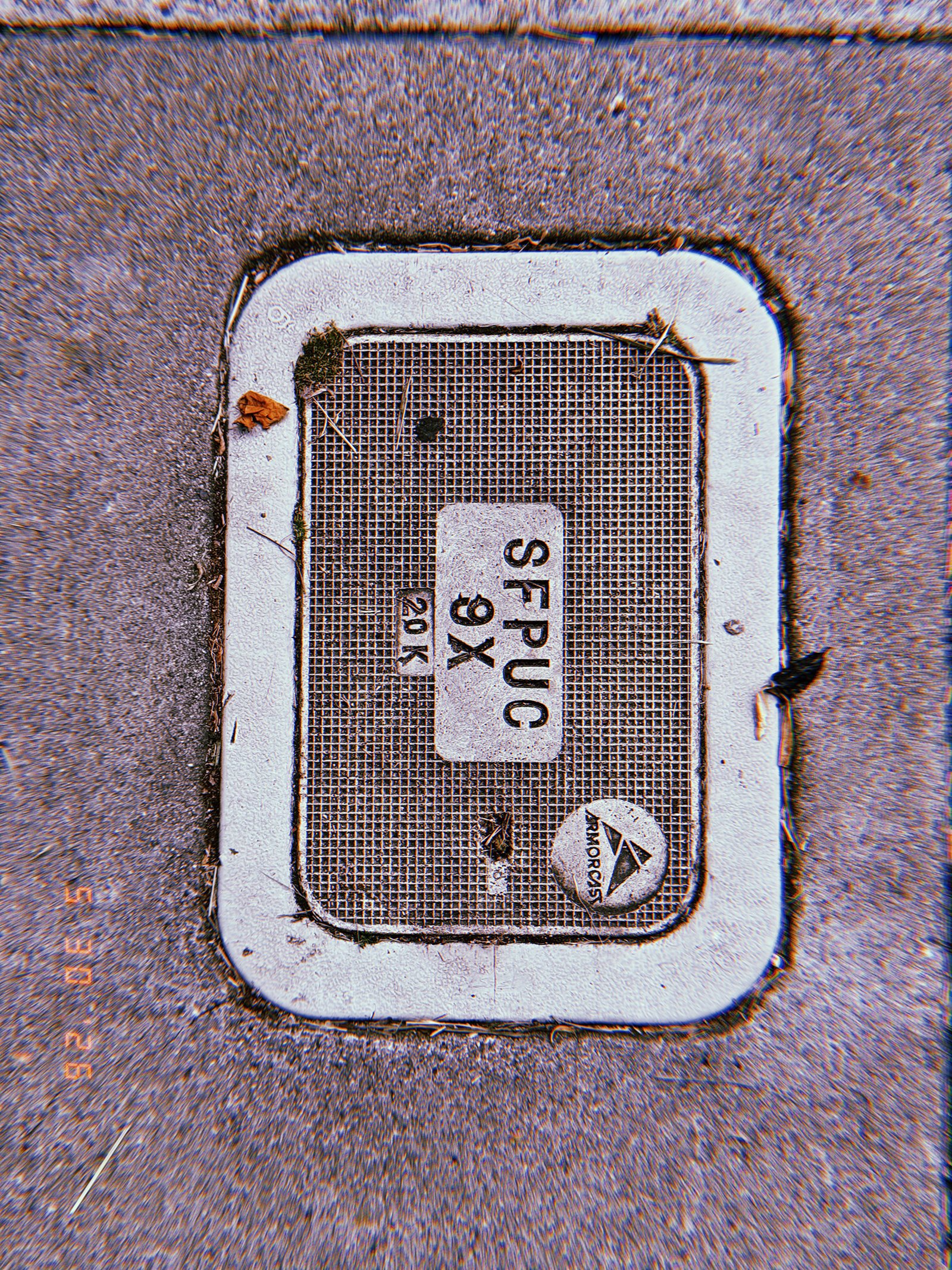 A rectangular communications access cover embedded in a concrete sidewalk. The textured utility panel contains identification markings and provides maintenance access to underground communication infrastructure.