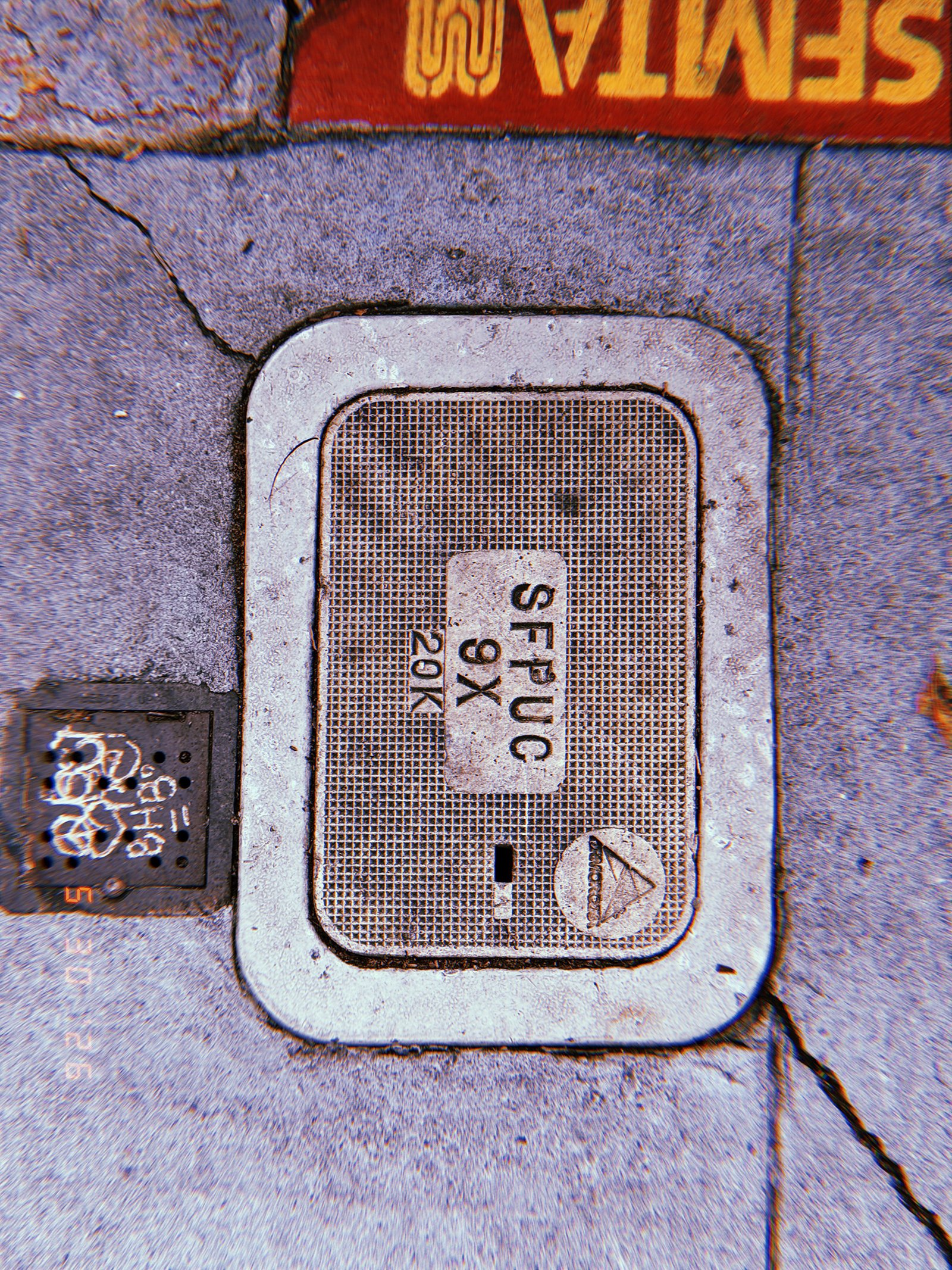 A rectangular communications access cover embedded in a concrete sidewalk. The textured utility panel contains service markings and provides maintenance access to underground communication infrastructure.