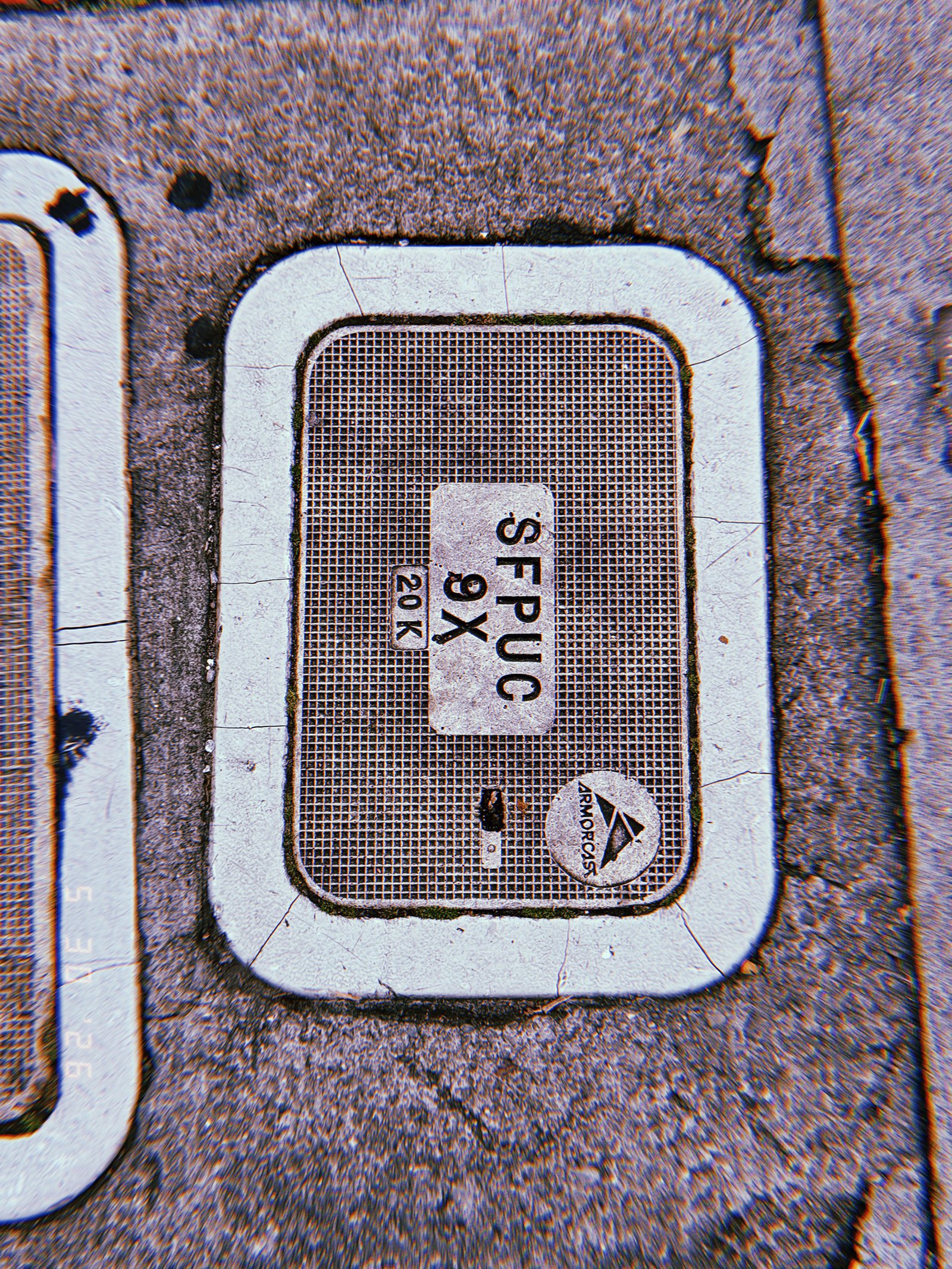 A rectangular communications access cover embedded in a concrete sidewalk. The textured lid displays service identification labels and utility markings, providing maintenance access to underground network infrastructure.