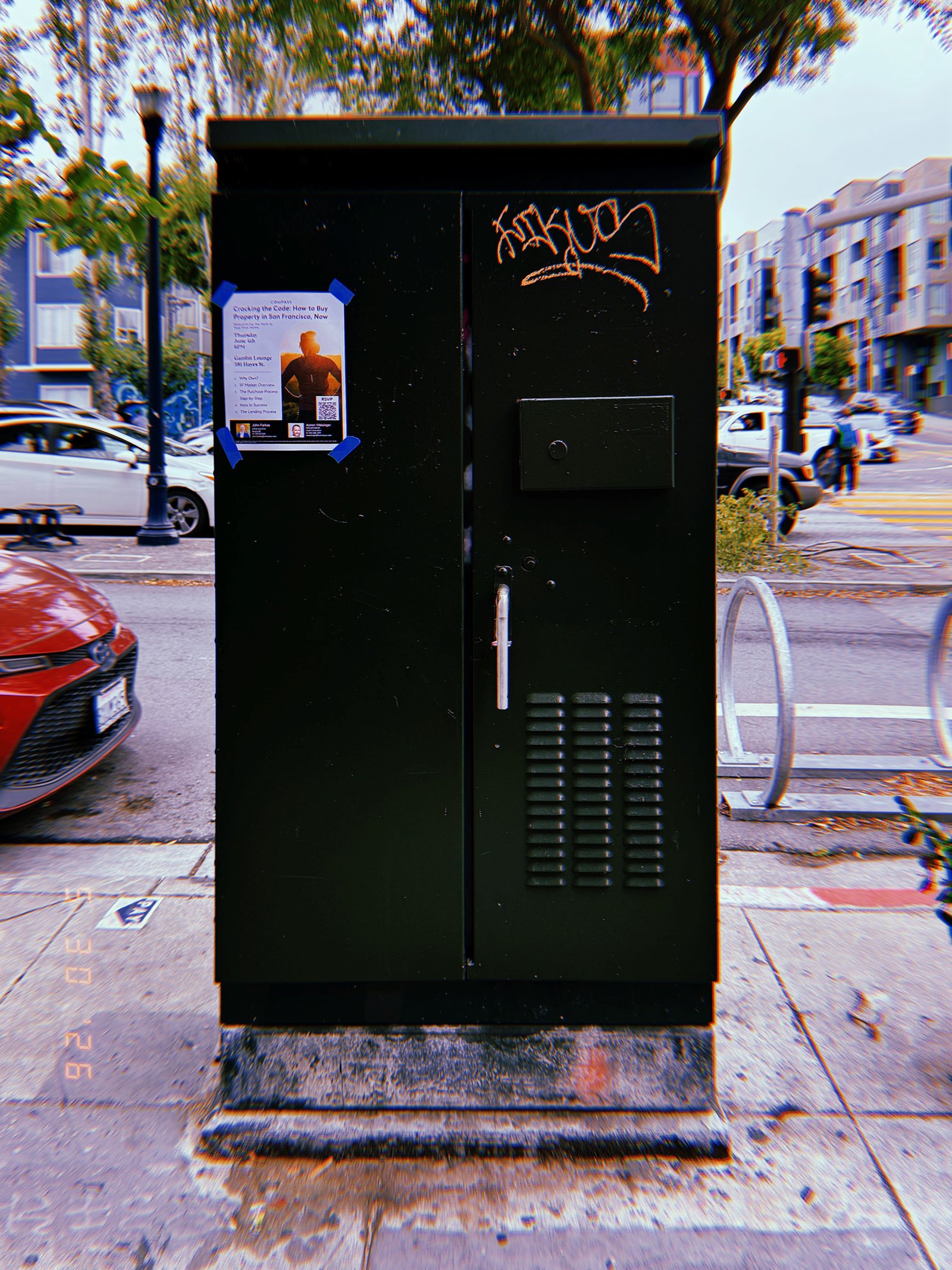 A black utility cabinet installed on a San Francisco sidewalk, marked with a posted flyer and graffiti while enclosing electrical or communications infrastructure.